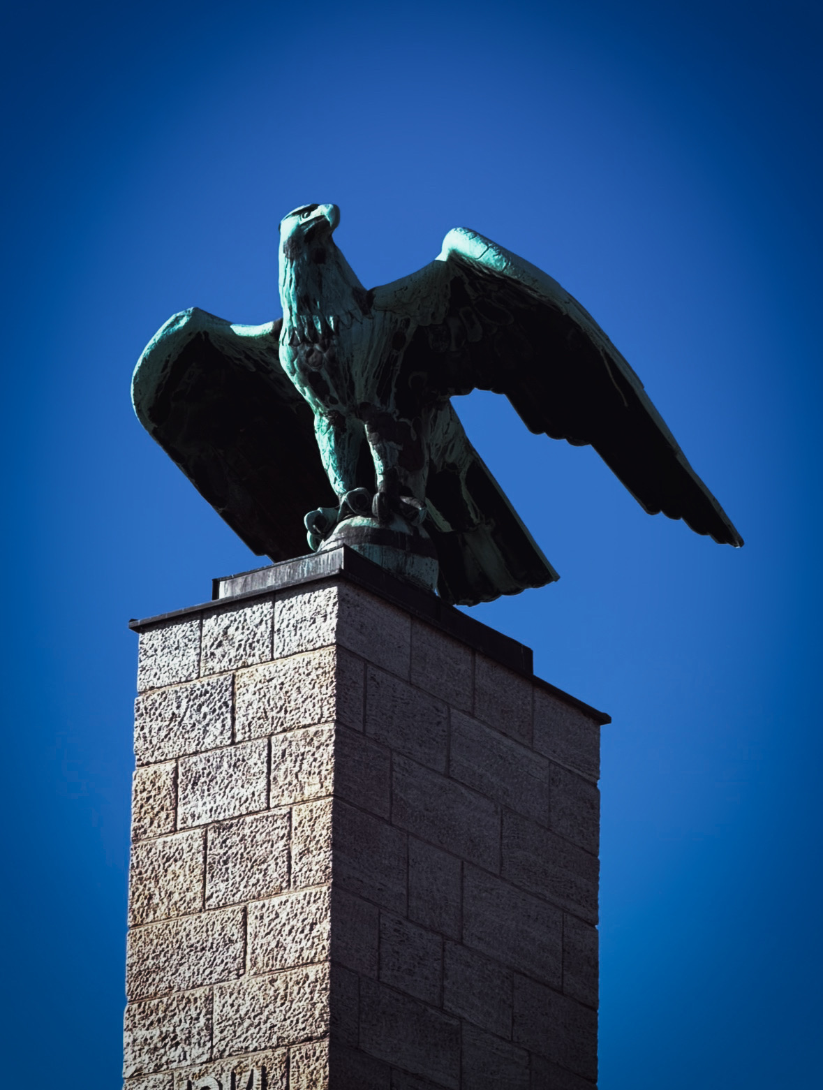 Bronze eagle statue on a tall stone pillar against blue sky